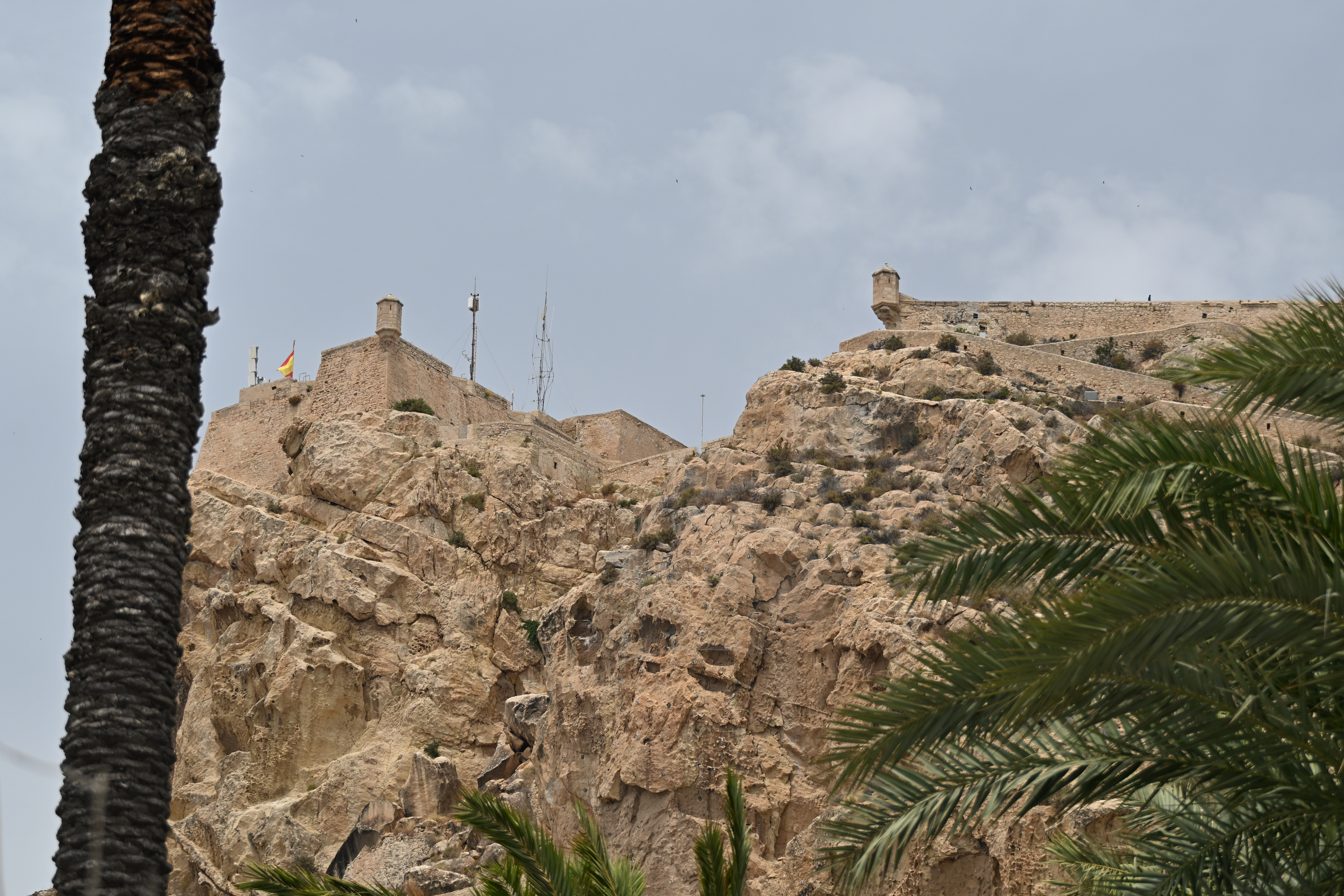 Burg Santa Bárbara auf dem felsigen Monte Benacantil in Alicante, eingerahmt von Palmen unter leicht bewölktem Himmel